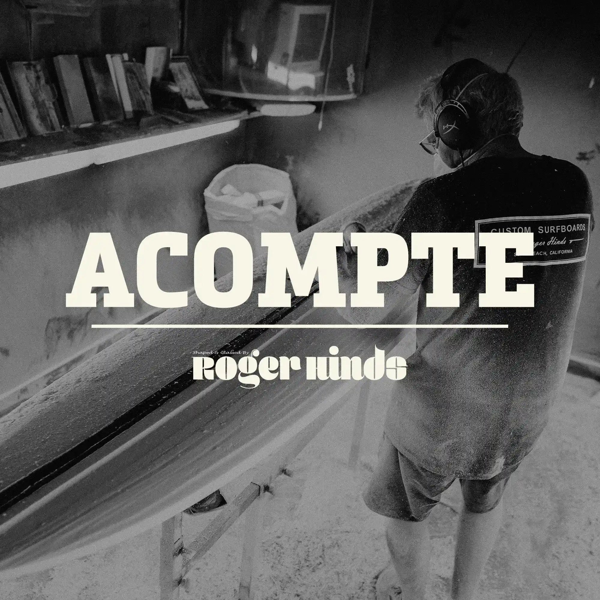 Shapers-Club- Dans un atelier faiblement éclairé, un individu masqué et portant un casque audio façonne minutieusement une planche de surf. Les mots « Acompte deposite - Roger Hinds » sont bien visibles, soulignant le travail artisanal en cours. -surfshop-surfboard