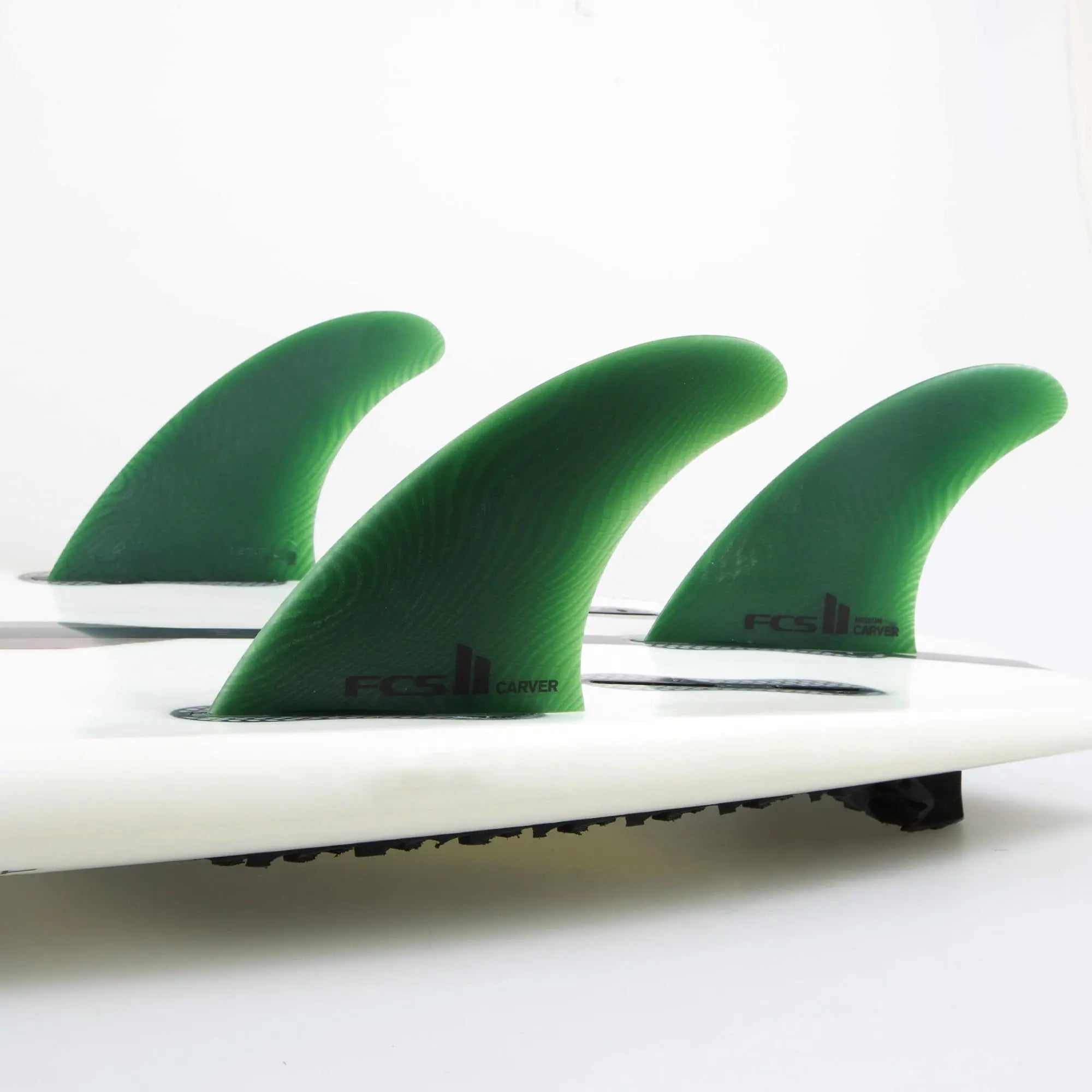Shapers-Club- Gros plan de trois grandes dérives vertes FCS Ⅱ Carver (Neo Glass Eco) dans une configuration de propulseur fixée à une planche de surf blanche. -surfshop-surfboard