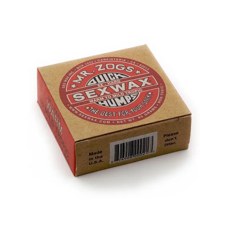 Shapers-Club- Une boîte en carton de Sexwax - Warm Tropical, idéale pour les ondulations tropicales chaudes, comporte une étiquette rouge et blanche indiquant « Le meilleur pour votre bâton ». L'emballage comporte un code-barres ainsi que des rappels : « Veuillez ne pas jeter de détritus » et « Fabriqué aux États-Unis ». -surfshop-surfboard