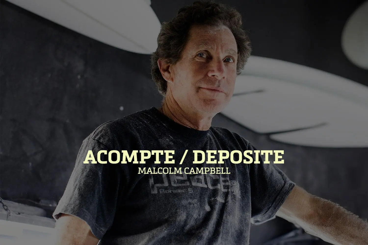 Shapers-Club- Dans une pièce faiblement éclairée, une personne en t-shirt sombre regarde la caméra. Les mots « Acompte deposite - Campbell Brothers » ressortent bien, évoquant l'héritage légendaire des frères Campbell. -surfshop-surfboard