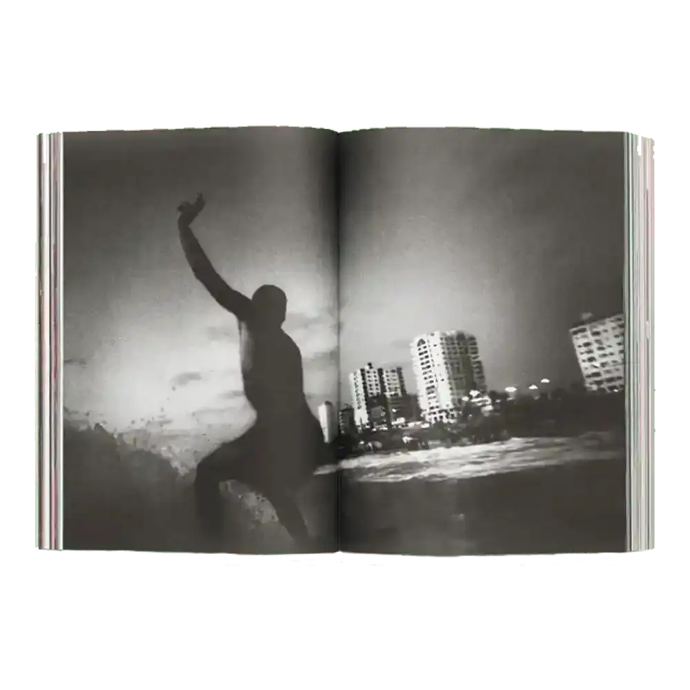 Shapers-Club- Un exemplaire ouvert d'ACID MAGAZINE - N°6 - WHATEVER SURFING MEANS présente une photo de surf en noir et blanc : un surfeur surfe sur une vague près des gratte-ciel de la ville sous un ciel nuageux. -surfshop-surfboard