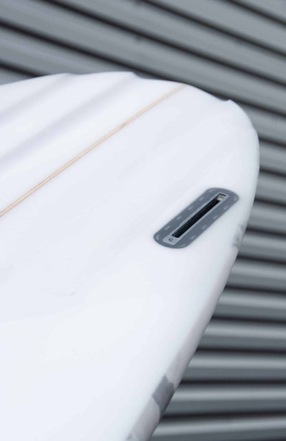 Shapers-Club- Gros plan de la queue d'une planche de surf blanche Aphex 6'10" x 20' 3/4" x 2' 3/4", mettant en valeur son boîtier à aileron unique, avec un revêtement en métal ondulé gris en arrière-plan. -surfshop-surfboard