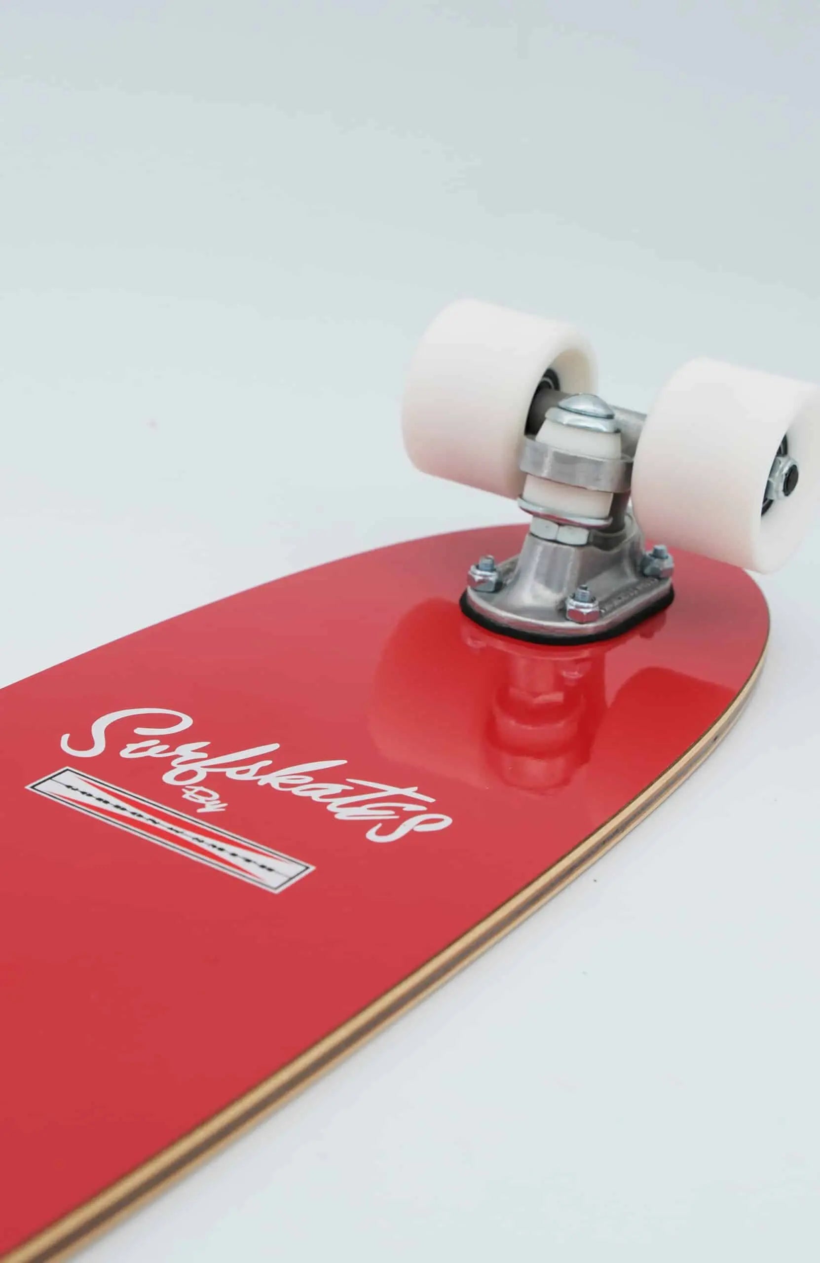 Shapers-Club- Gros plan du Gordon & Smith 25" Rouge Cerise SurfSkate complet, avec roues blanches, trucks argentés et un logo en script blanc et un graphisme rappelant les designs classiques. Le skateboard est incliné sur une surface blanche. -surfshop-surfboard