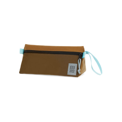 Shapers-Club- La trousse de toilette TOPO en Desert Palm et Pond Blue est une pochette rectangulaire avec une surface en tissu lisse. Elle est dotée d'une fermeture à glissière horizontale sur le dessus, d'une dragonne bleu clair rappelant Pond Blue attachée sur un côté et d'une petite étiquette grise avec du texte dans le coin inférieur droit. -surfshop-surfboard