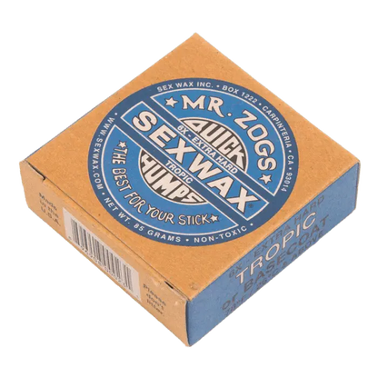 Shapers-Club- Une petite boîte carrée en carton beige et bleu de cire de surf extra dure « Mr. Zog's Sexwax » Tropic, commercialisée sous le nom de « Sexwax - Tropic Basecoat », comporte un marquage circulaire sur le dessus et un code-barres avec des détails textuels sur le côté. La boîte indique qu'elle est « la meilleure pour votre planche », pèse 85 grammes et peut être utilisée comme couche de base Tropic. -surfshop-surfboard