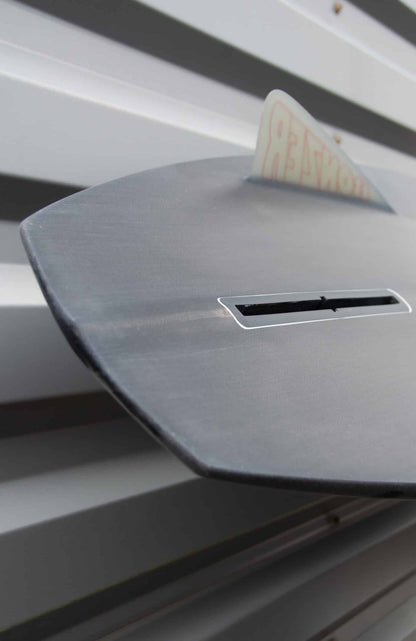 Shapers-Club- Gros plan d'une boîte aux lettres à enveloppe grise avec vue partielle d'une enveloppe blanche partiellement insérée. La boîte aux lettres, dont le design reflète les lignes épurées caractéristiques de la planche de surf Campbell Brothers - Russ Short 7'0" x 20' 3/4" x 2' 3/4", est montée sur une surface métallique à nervures horizontales. -surfshop-surfboard