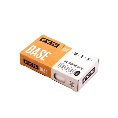 Shapers-Club- Une boîte en carton rectangulaire étiquetée « FCS - Wax - Base » conçue pour les planches de surf. La boîte est principalement marron et blanche avec un texte noir, indiquant que la cire convient à toutes les températures. Un petit trou sur un côté révèle la cire de base blanche à l'intérieur. -surfshop-surfboard