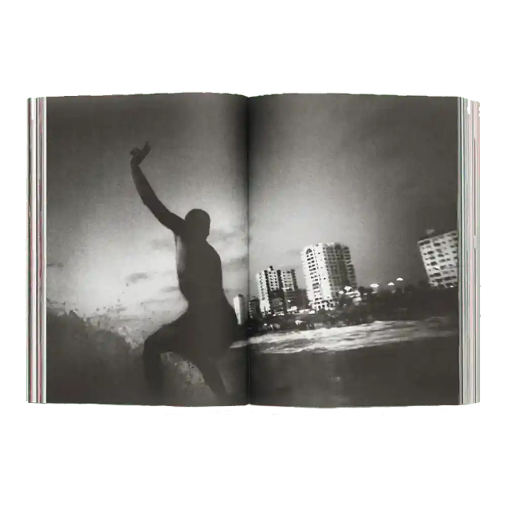 Shapers-Club- Un exemplaire ouvert d'ACID MAGAZINE - N°6 - WHATEVER SURFING MEANS présente une photo de surf en noir et blanc : un surfeur surfe sur une vague près des gratte-ciel de la ville sous un ciel nuageux. -surfshop-surfboard