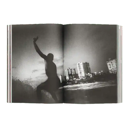 Shapers-Club- Un exemplaire ouvert d'ACID MAGAZINE - N°6 - WHATEVER SURFING MEANS présente une photo de surf en noir et blanc : un surfeur surfe sur une vague près des gratte-ciel de la ville sous un ciel nuageux. -surfshop-surfboard